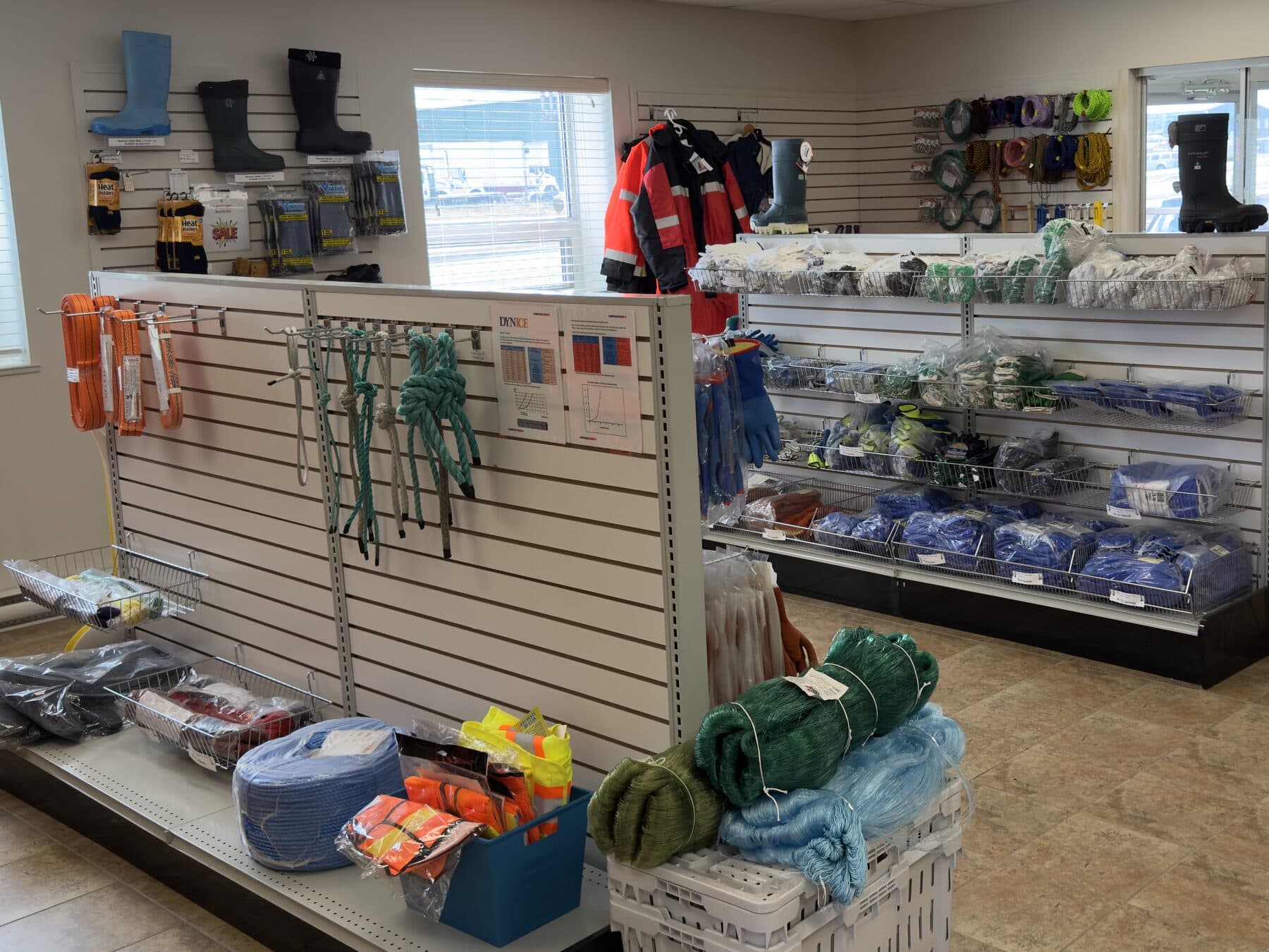 The Paradise sales floor — boots and packaged gear on the wall, webbing slings and spliced rope hanks hung along the slatwall, with coiled rope, hi-vis vests and green and blue netting in the foreground