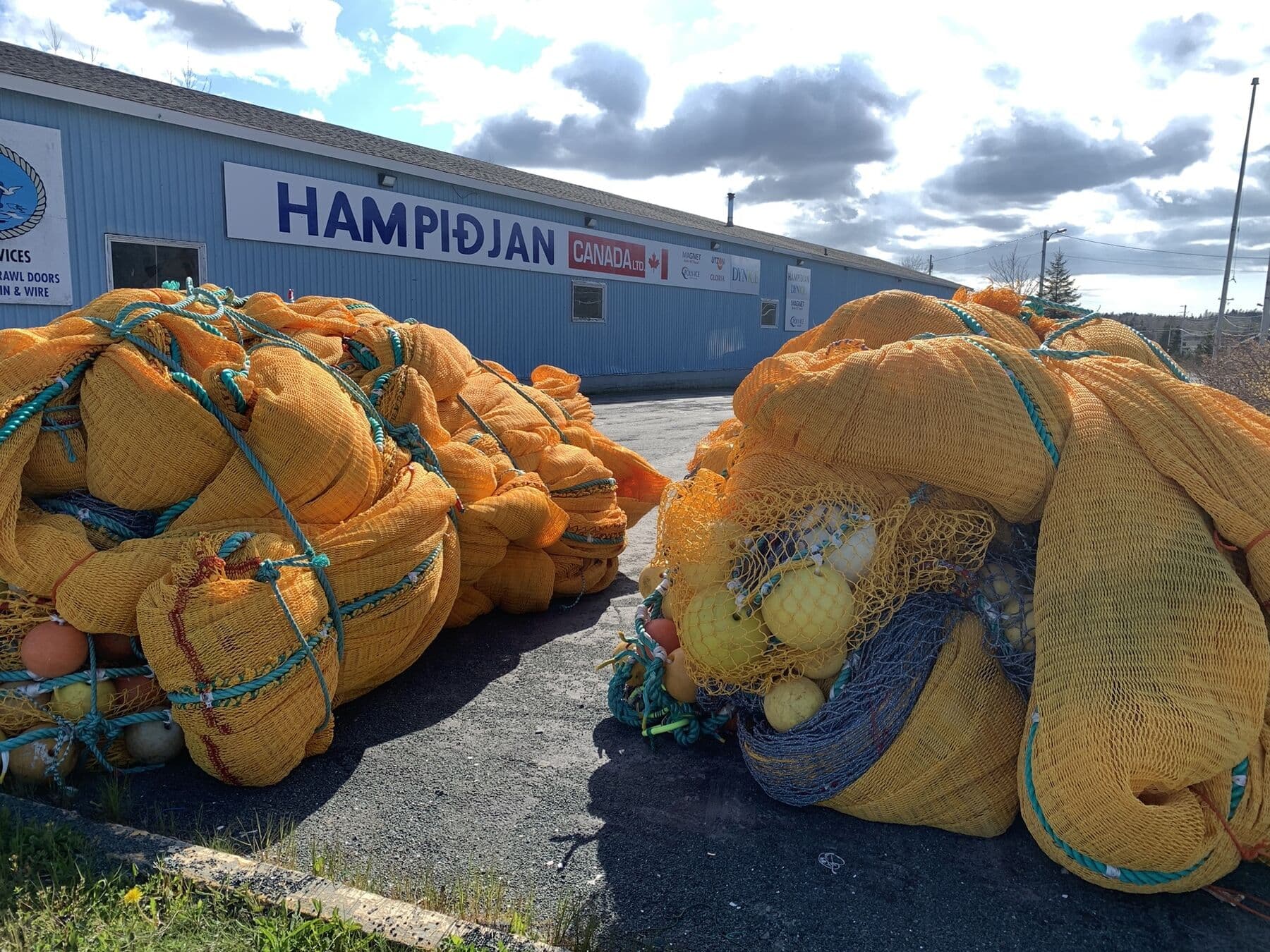 Bundled orange trawls stacked on the apron outside the Spaniard's Bay branch, the Hampidjan Canada sign on the blue building behind them