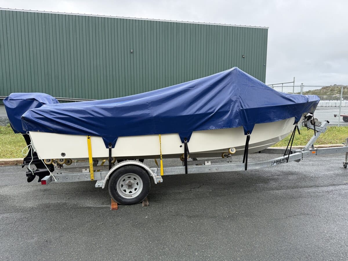 An open boat on its trailer under a fitted navy cover, drawn down over the gunwales and strapped along the hull.