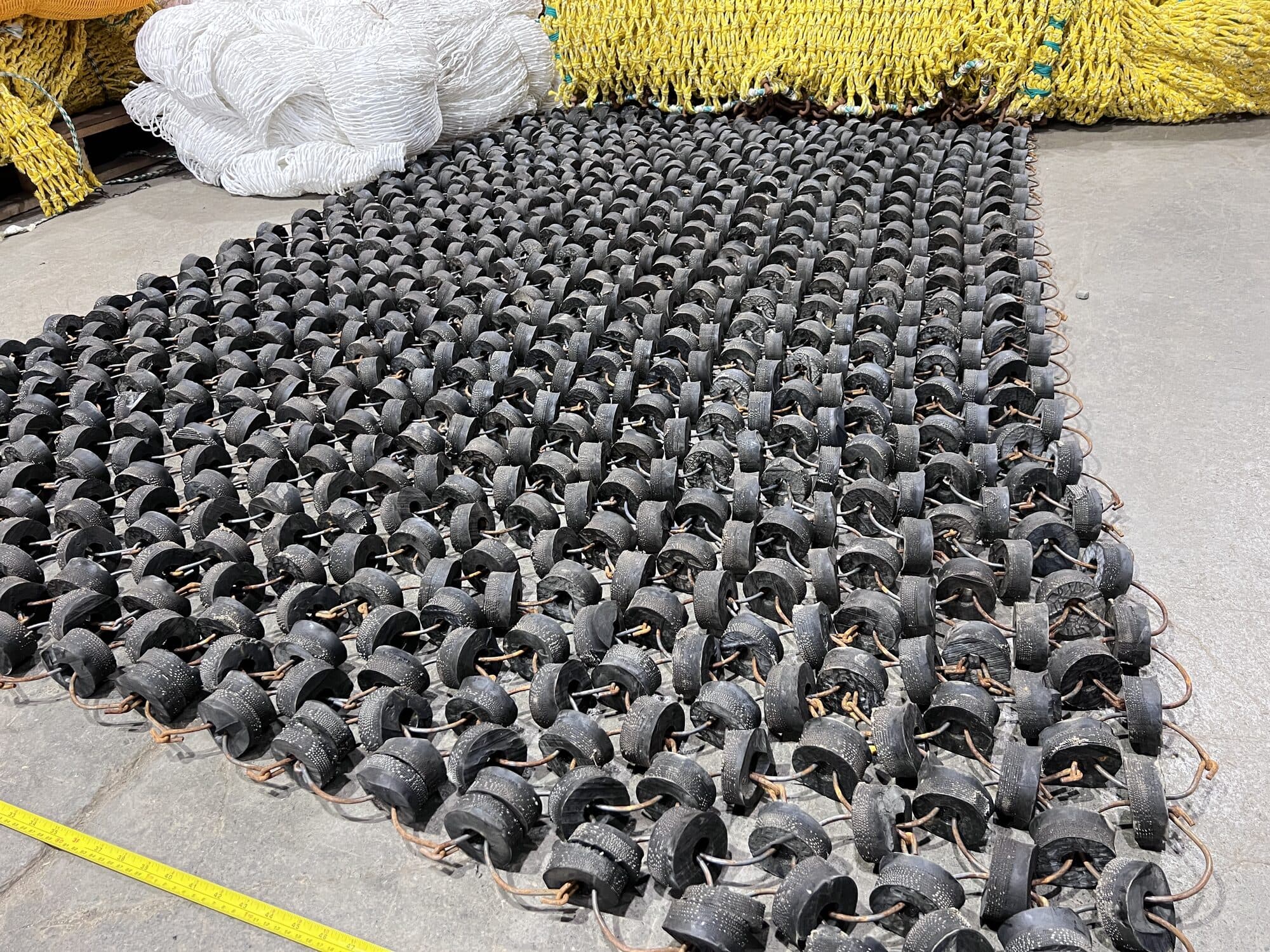 Rubber disc groundgear laid out flat on the shop apron with a yellow tape measure along the near edge, white and yellow netting stacked behind it