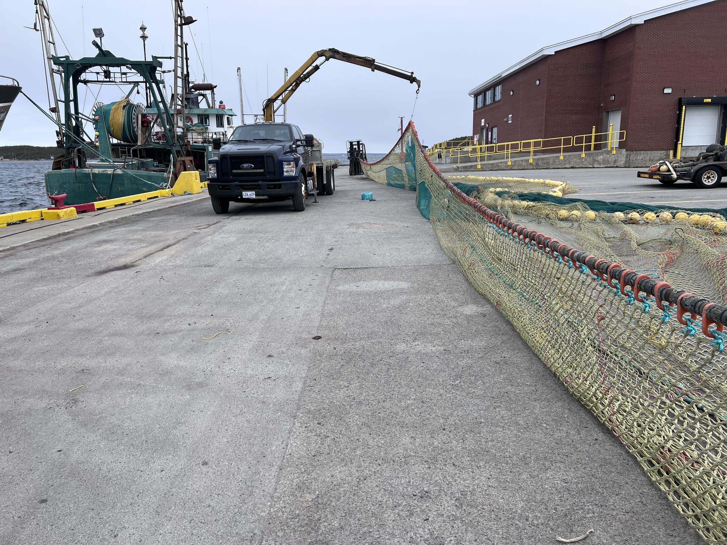 Gear laid out the length of the apron at the Port au Choix branch, a boom truck alongside and a green-hulled trawler waiting at the wharf