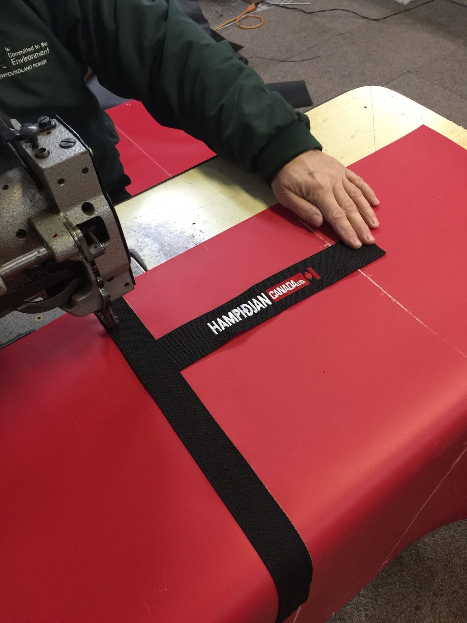 Branded webbing being stitched onto red PVC at the sewing machine