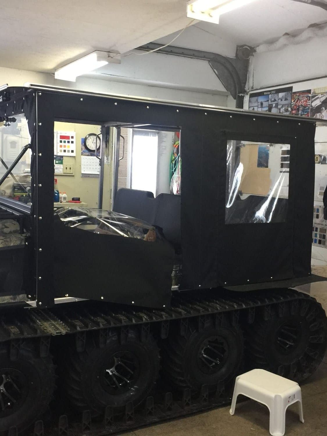 A tracked utility carrier fitted with a full black canvas cab, doors and windows in place