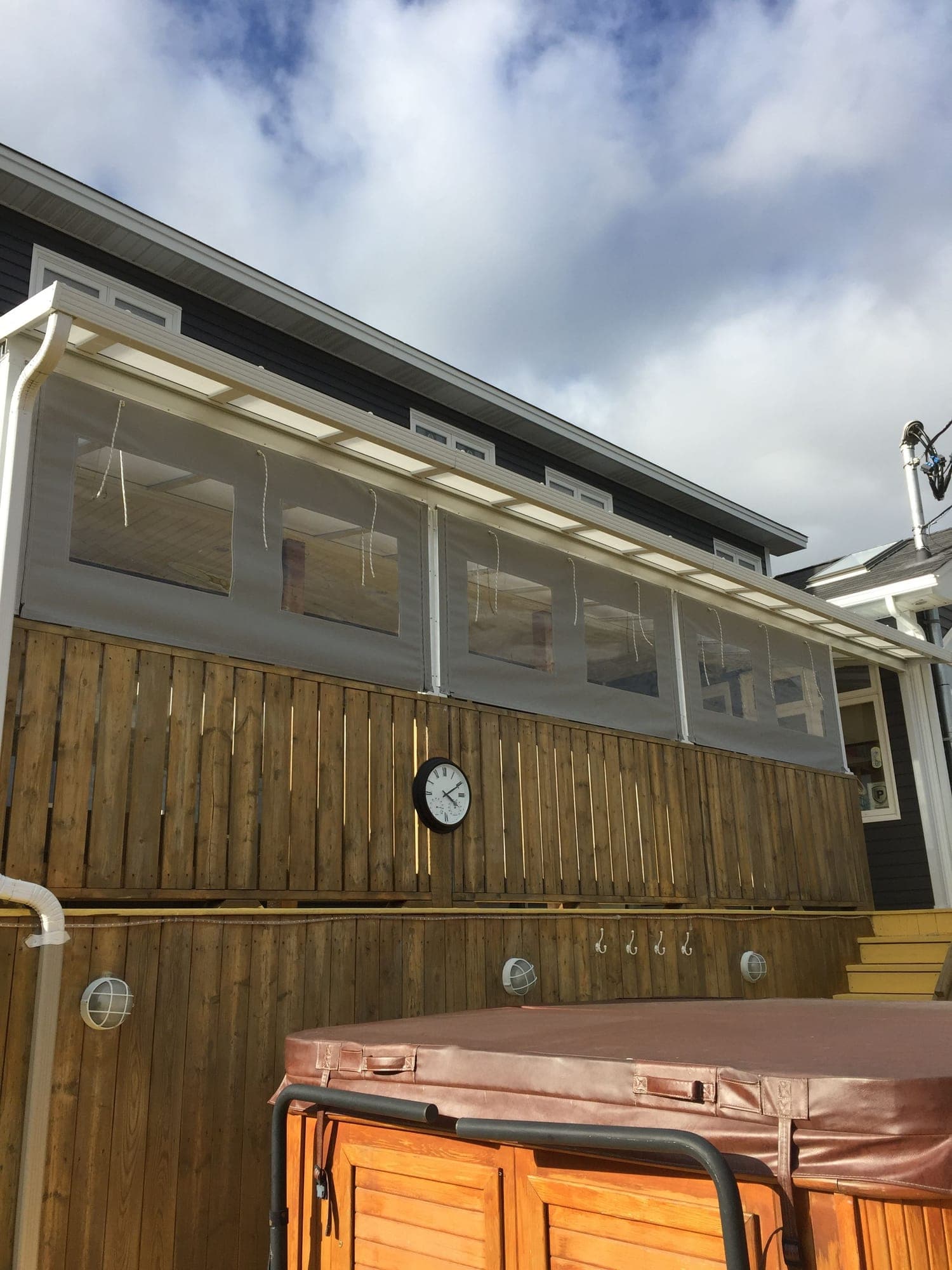 Canvas weather curtains with clear window panels, hung along the top of a wooden deck rail with their roll-up ties hanging loose
