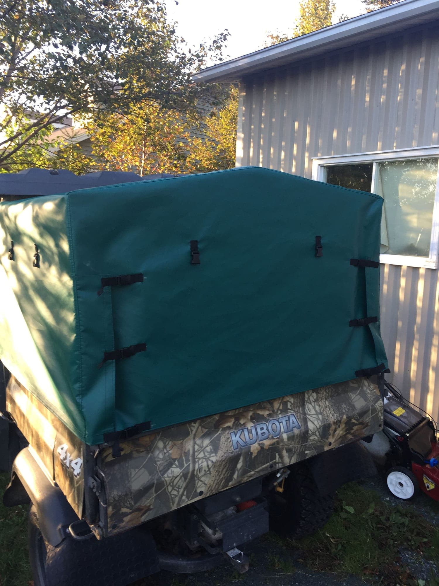 A fitted green cover strapped down over the cargo bed of a Kubota utility vehicle outside the shop
