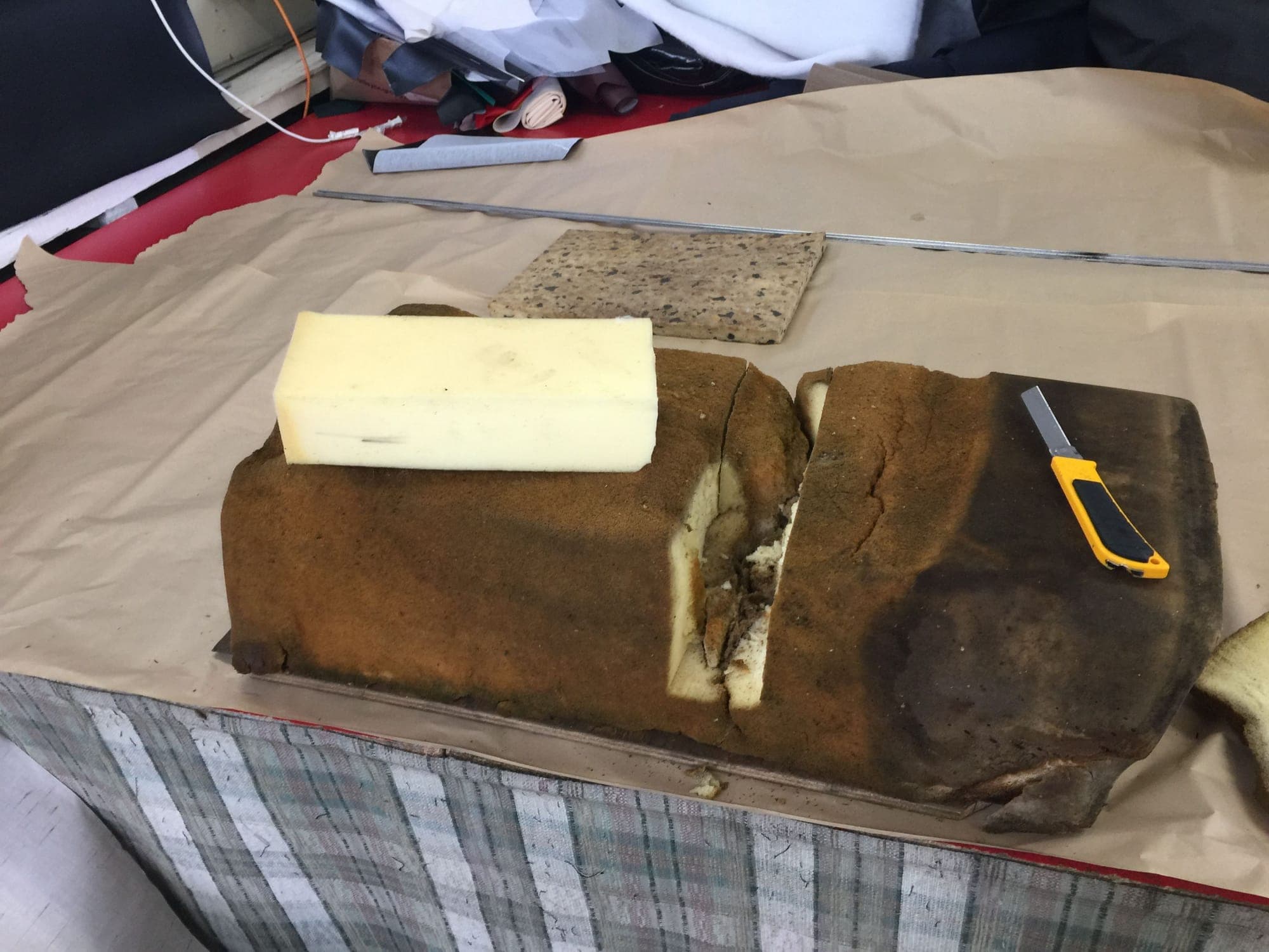 A seat base with the old brown foam cut open and a new block of white foam being fitted in, knife on the paper alongside