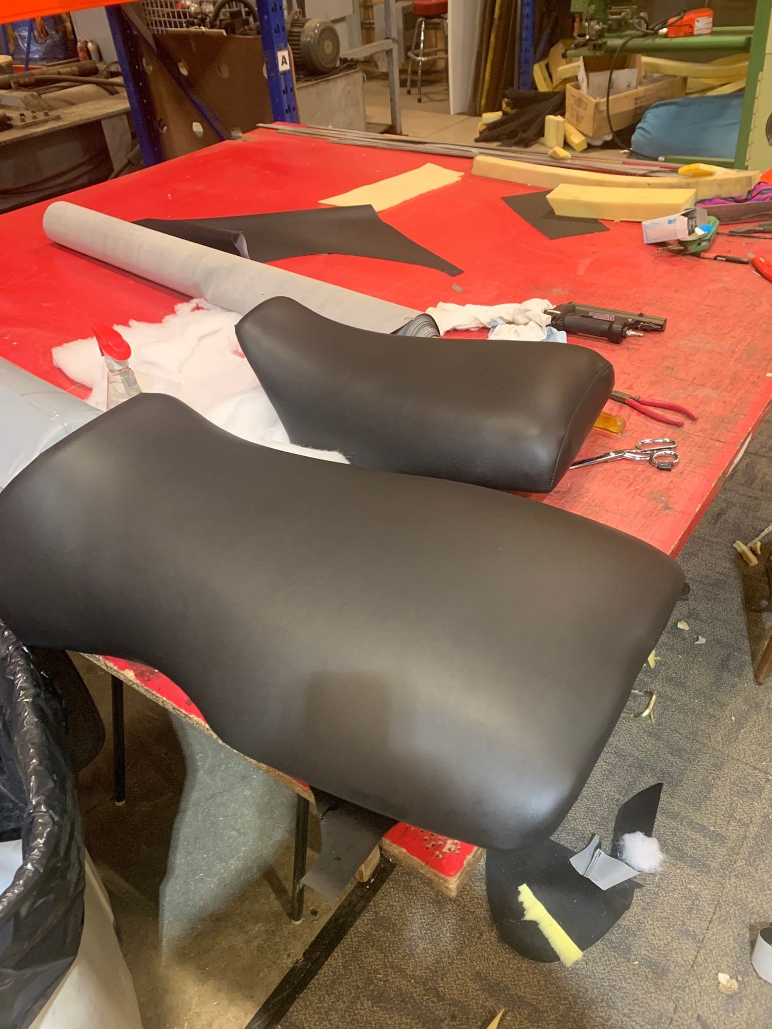The same two seats recovered in dark brown vinyl, the roll of material and the offcuts still on the bench