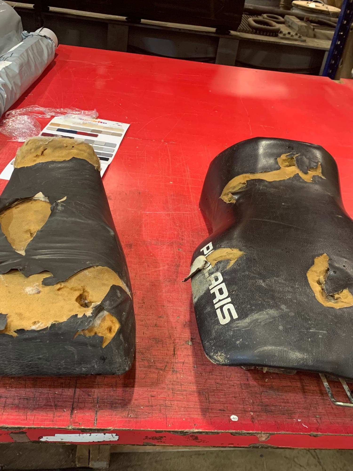 Two machine seats on the cutting table with the vinyl torn away and the foam underneath broken open