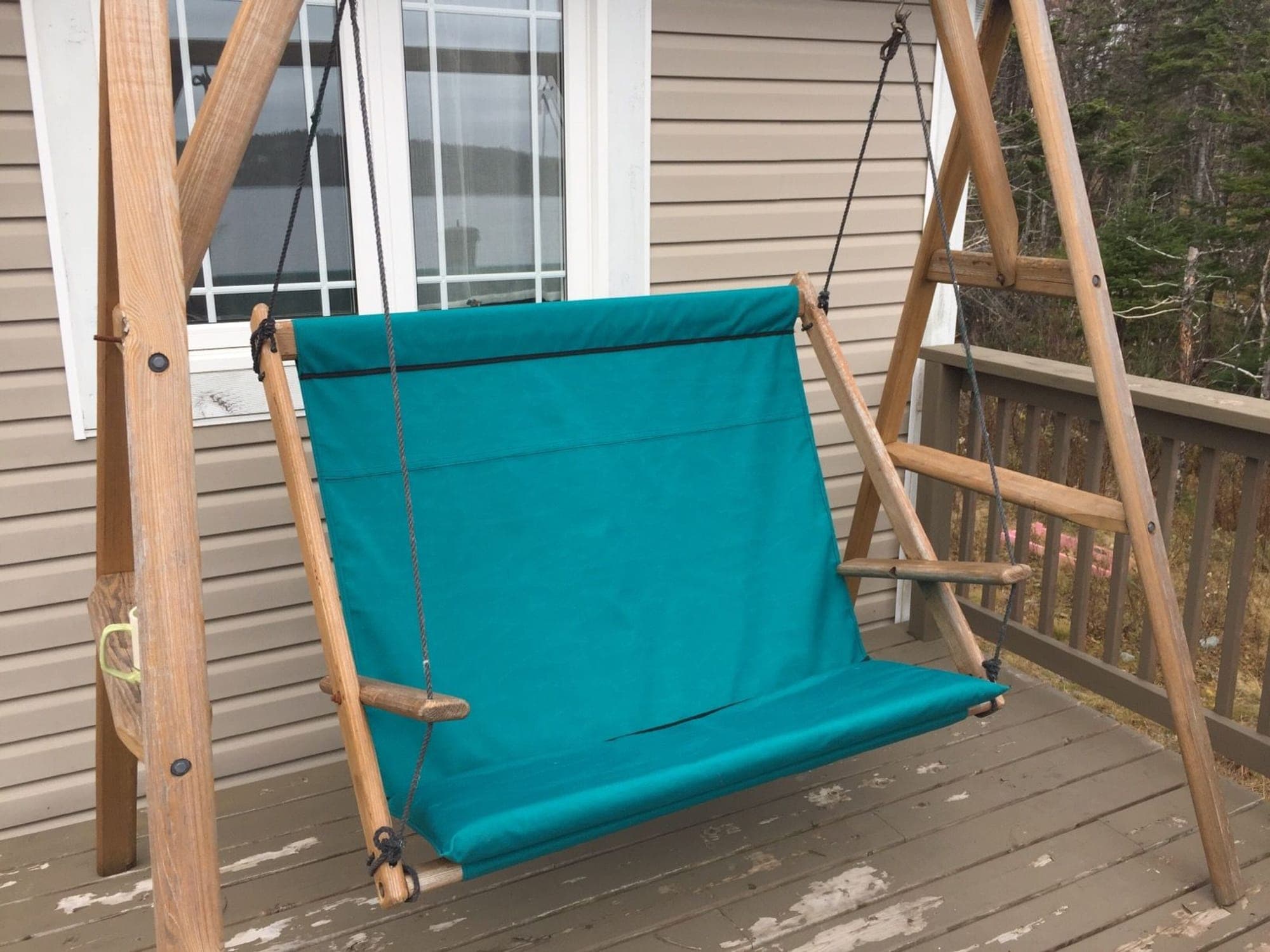 A teal canvas seat and back fitted to a wooden garden swing frame on a deck