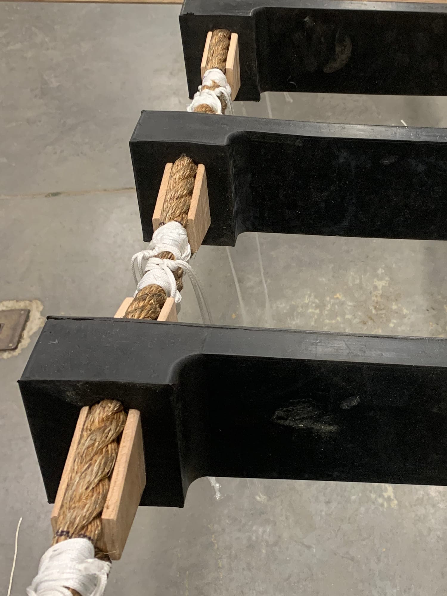 A rope ladder on the shop floor, Manila side ropes with timber chocks and white twine seizings holding each wide black step