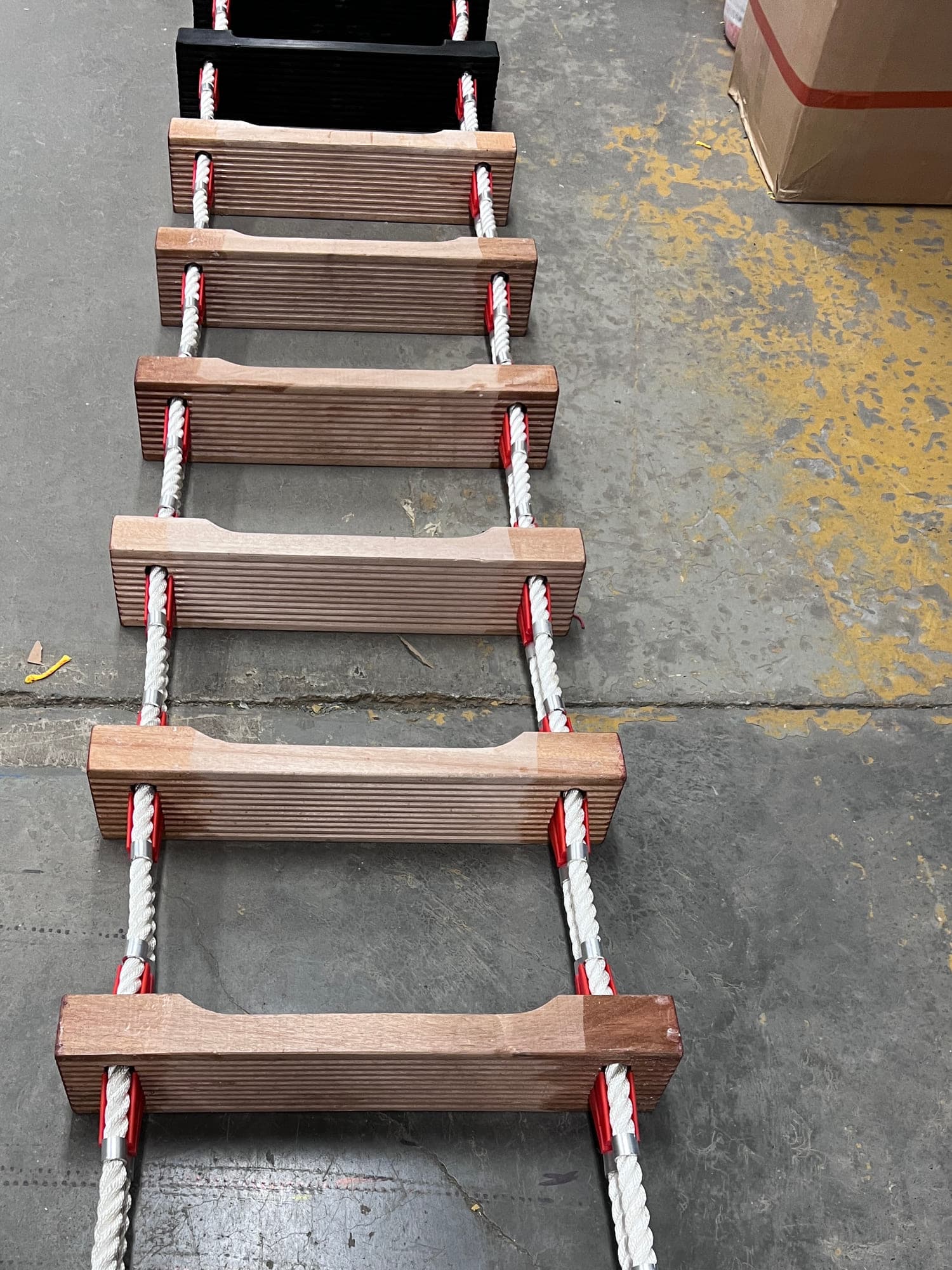 A pilot ladder running away down the shop floor, ribbed hardwood steps between white three-strand side ropes with red chocks and metal ferrules