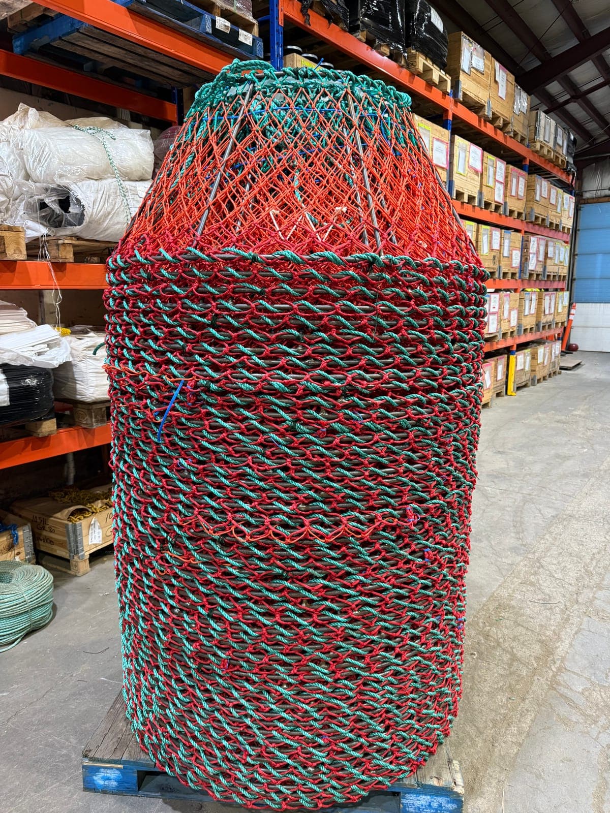 A large pot netted in red and green rope, standing on its pallet in the shop