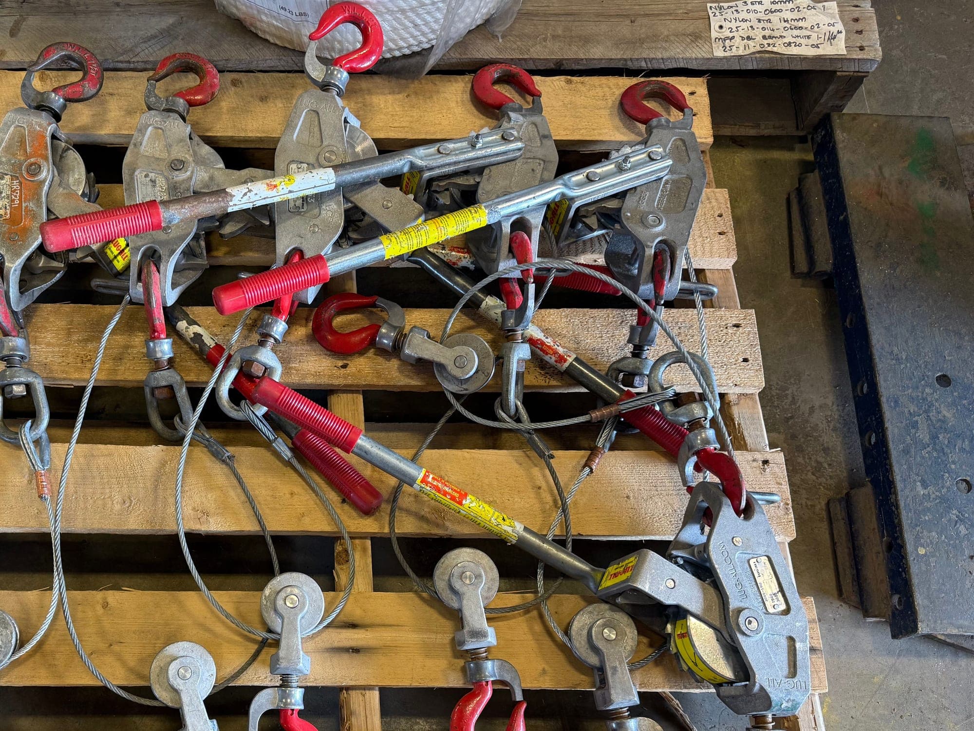 Wire rope pullers laid out on a pallet after inspection, hooks turned up and their wire ropes coiled clear