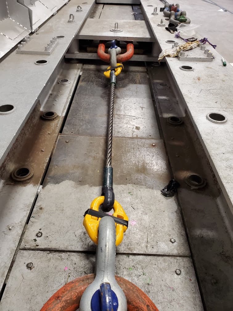 A wire rope assembly rigged the length of the test bed, a yellow master link and a bow shackle at each end joining it to the bed's anchor points