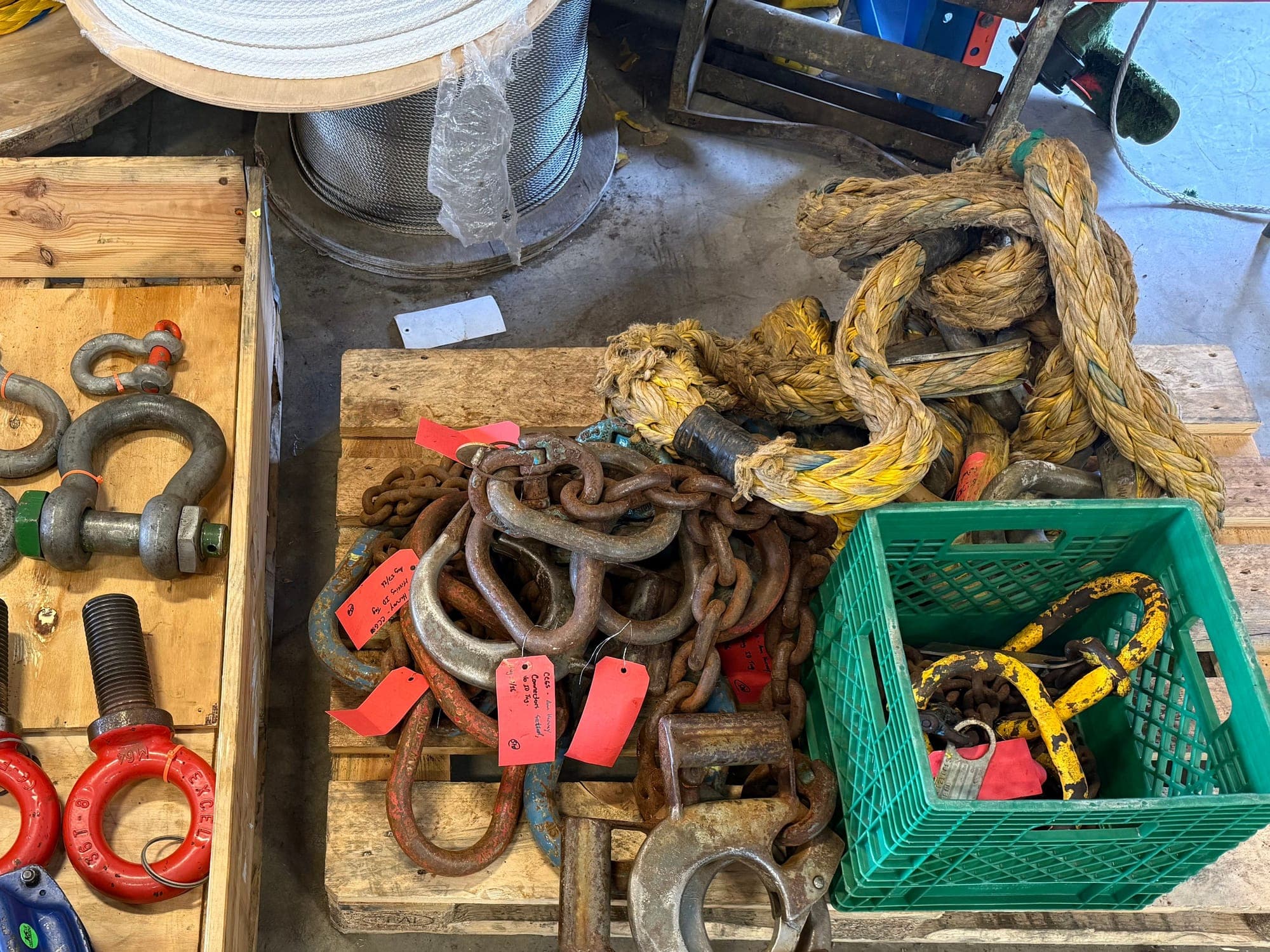 A pallet of chain, links and shackles carrying red inspection tags, with rope and lifting hooks alongside