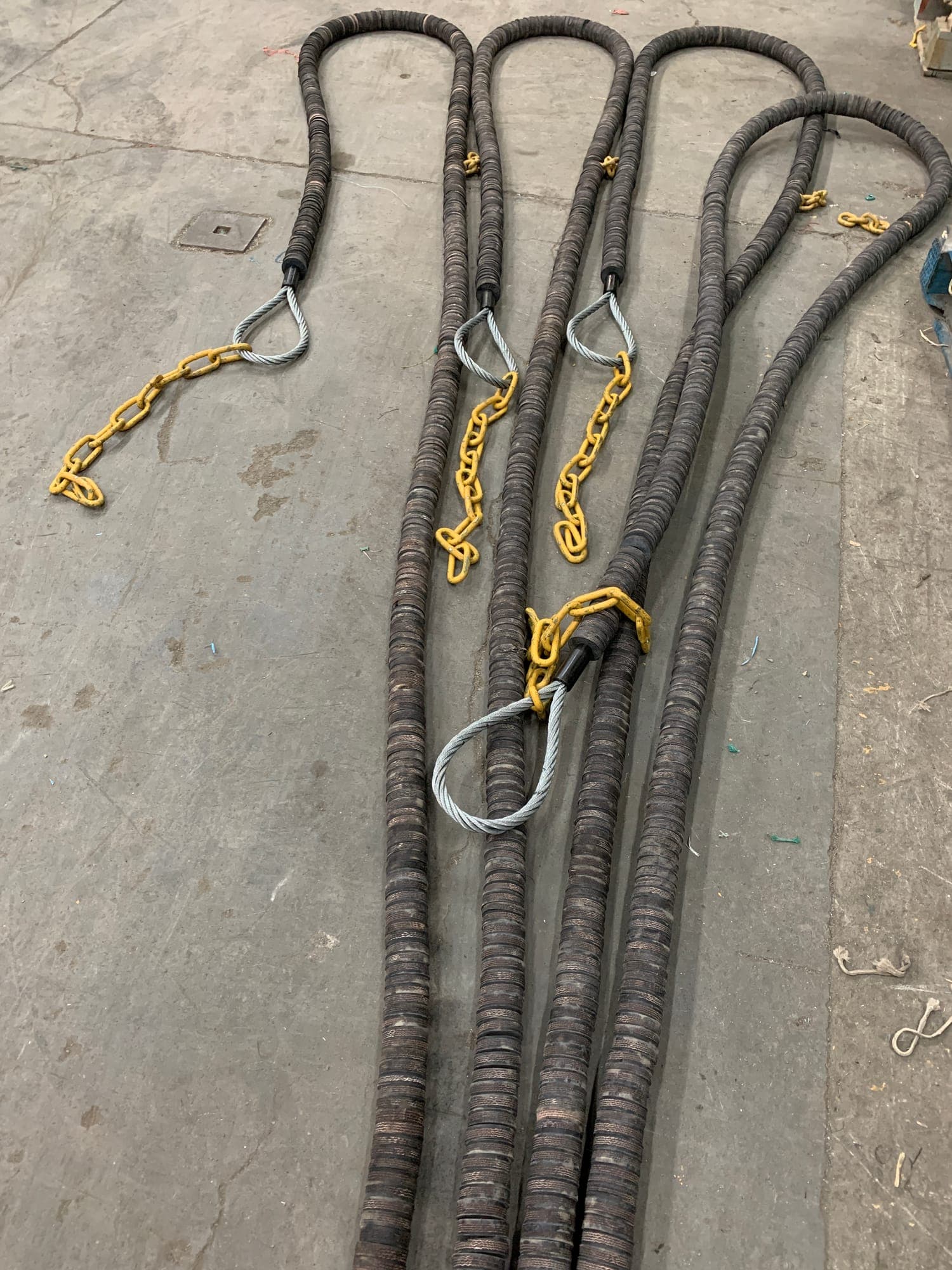 Four heavy wire legs on the shop floor, each sleeved in rubber spacers and finished with a soft eye and a chain tail
