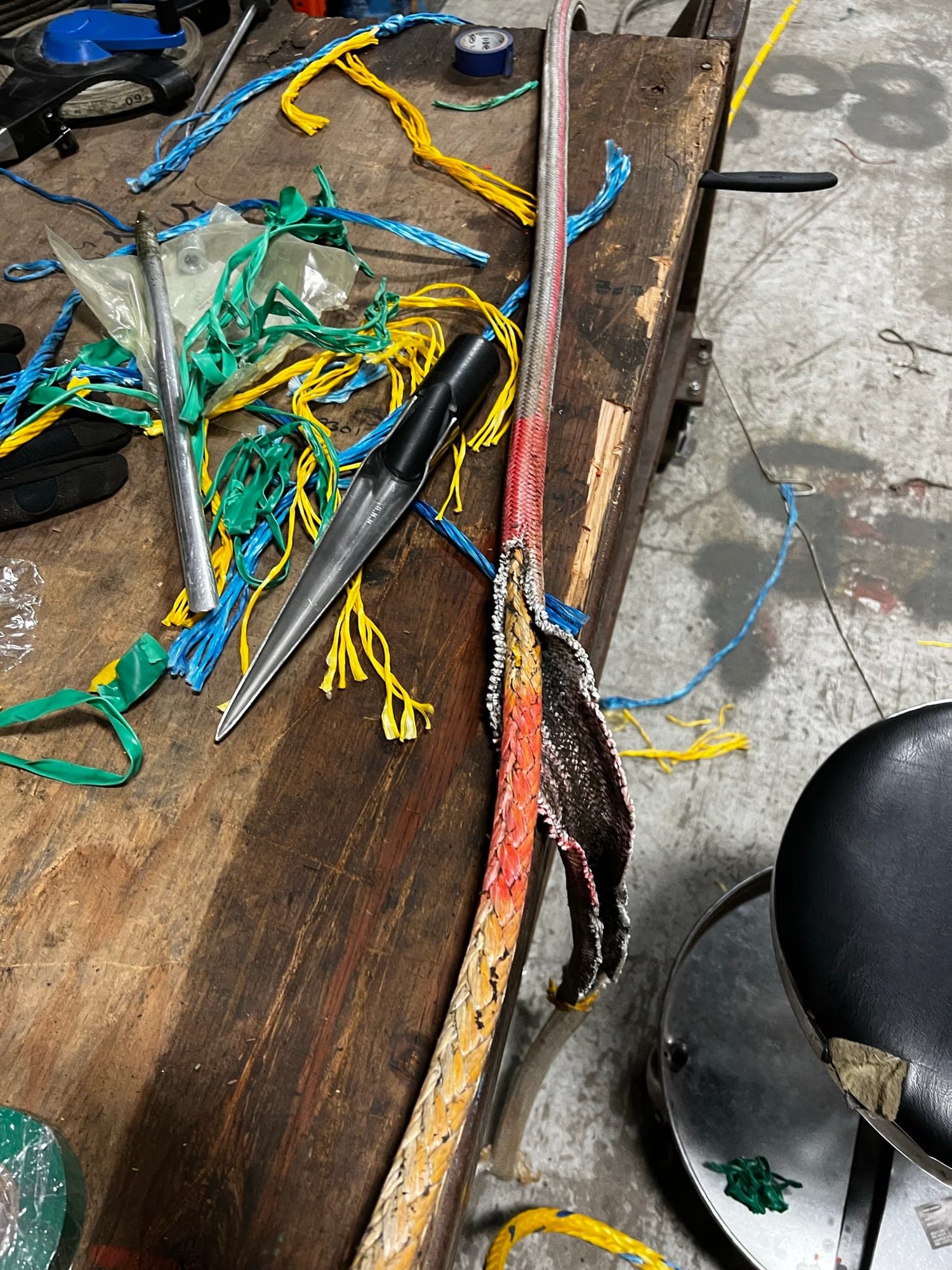 Steel fids on the splicing bench beside a rope with its cover peeled back, whipping twine scattered around them