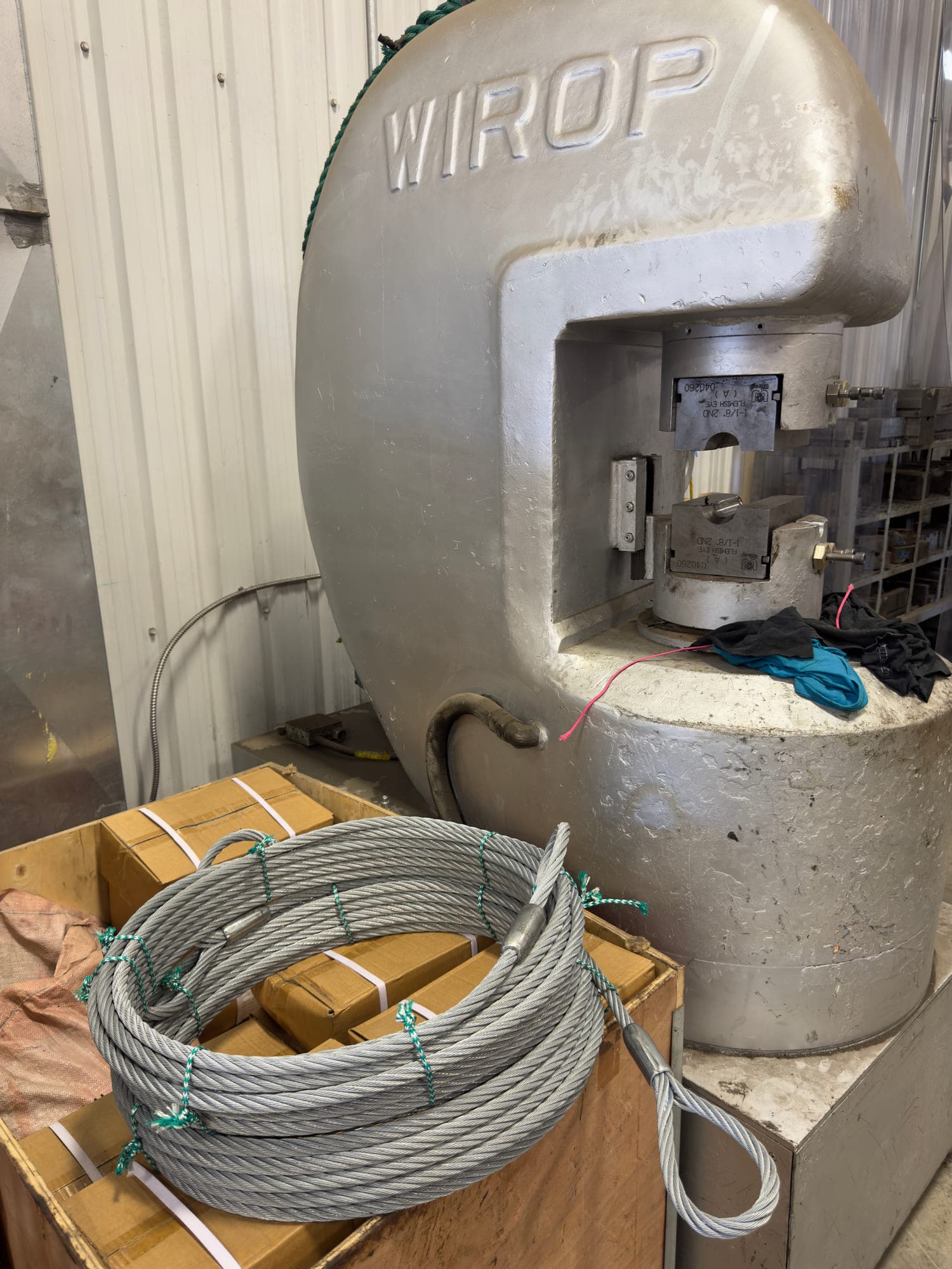 The WIROP swaging press on the shop floor with the dies open in its throat, a coiled wire assembly on the crate in front of it