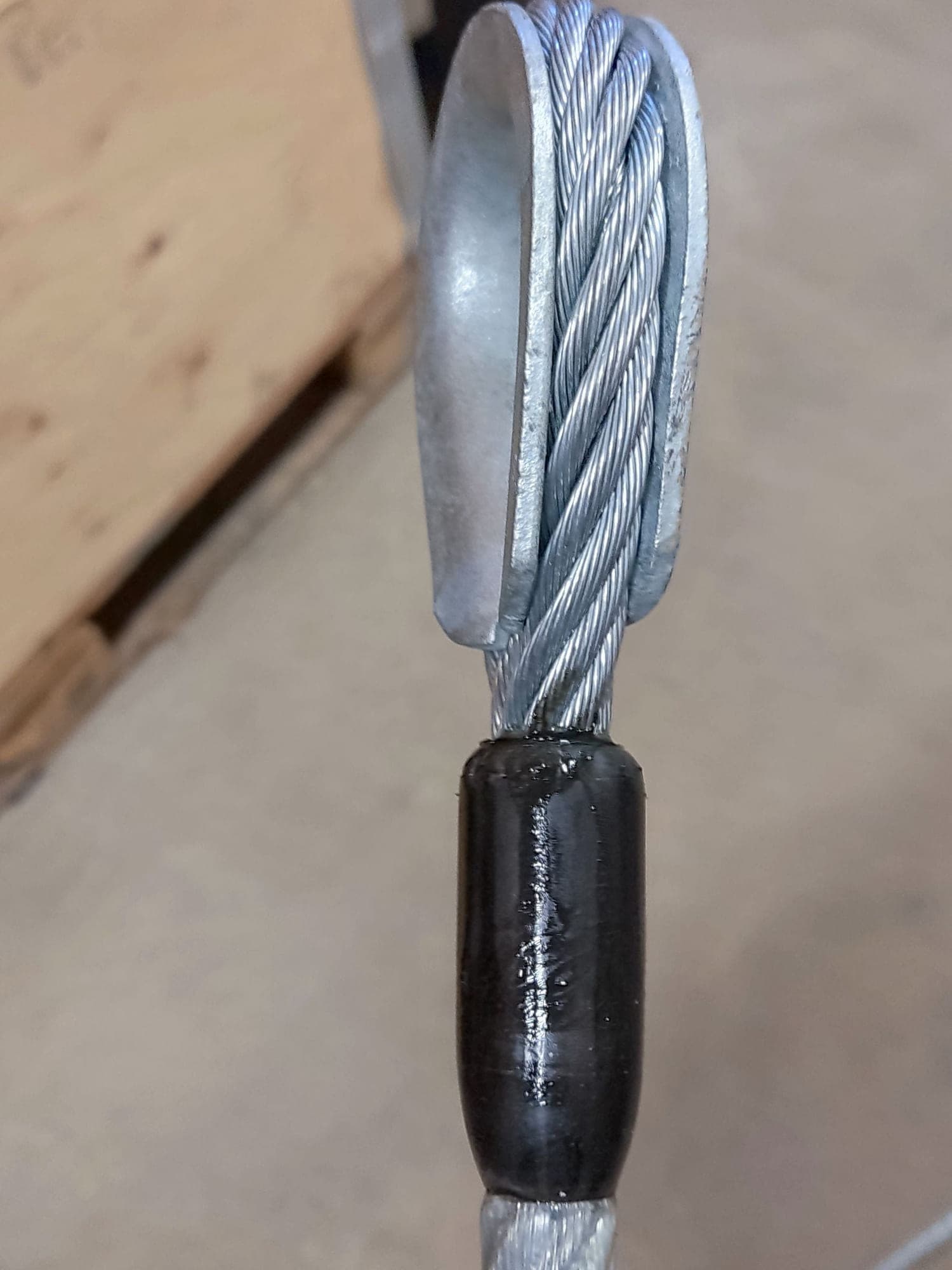 A wire rope eye seated in a galvanized thimble with a black steel ferrule pressed shut below it