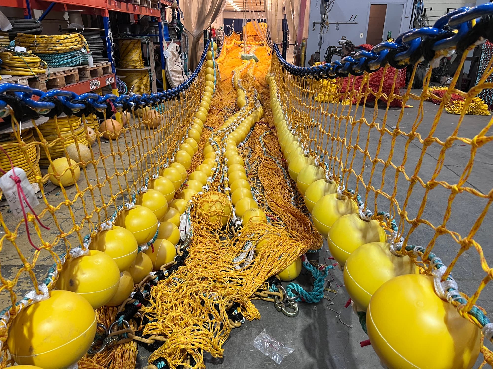 A trawl rigged out down the loft floor — floats on the headline, chain along the footrope, netting running the length of the aisle
