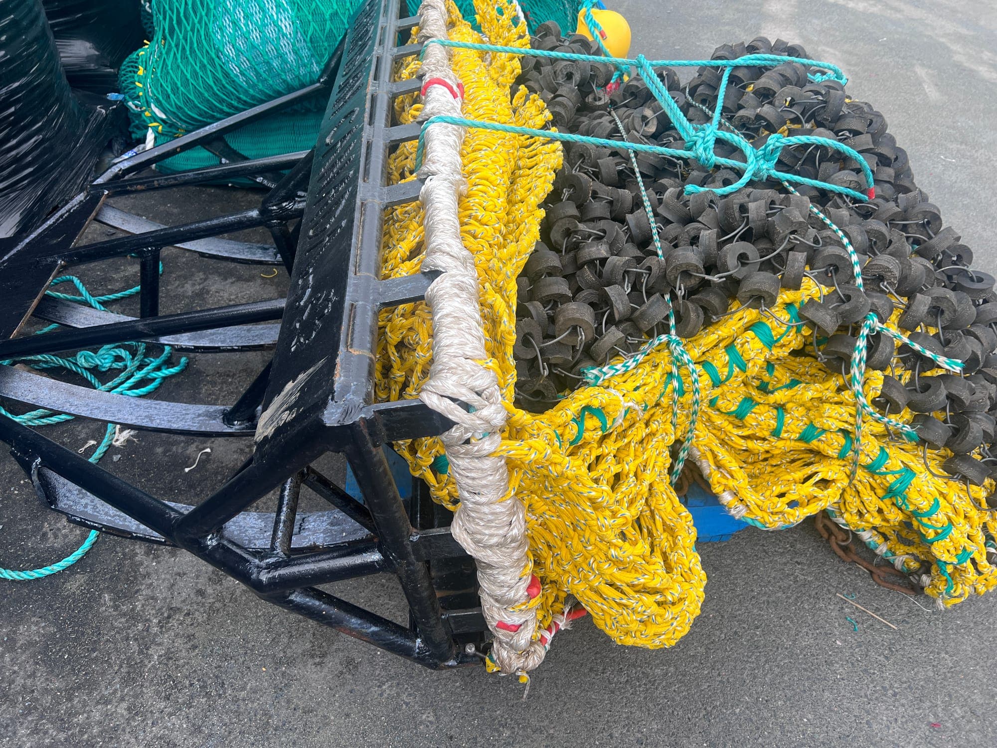 A finished dredge frame in black steel on the wharf with its netting and rockhopper gear bundled alongside